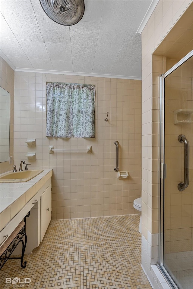 bathroom with tile walls, a stall shower, ornamental molding, and a sink
