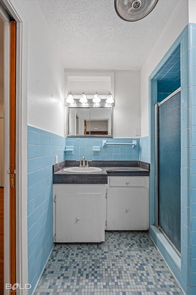full bathroom with tile walls, a wainscoted wall, vanity, a textured ceiling, and a stall shower
