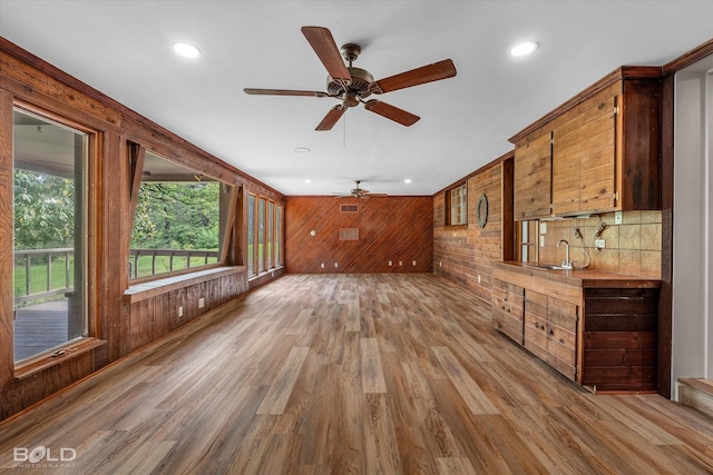 unfurnished living room featuring a sink, light wood-type flooring, wood walls, ceiling fan, and recessed lighting
