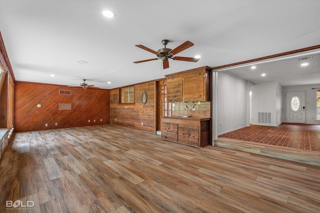 unfurnished living room with ceiling fan, wooden walls, visible vents, and wood finished floors