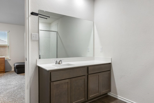 bathroom with a shower with shower door, vanity, a textured wall, and baseboards