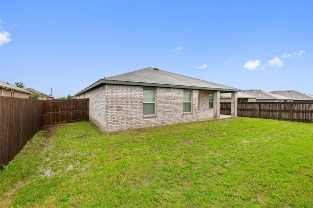 back of house with a yard, brick siding, and a fenced backyard