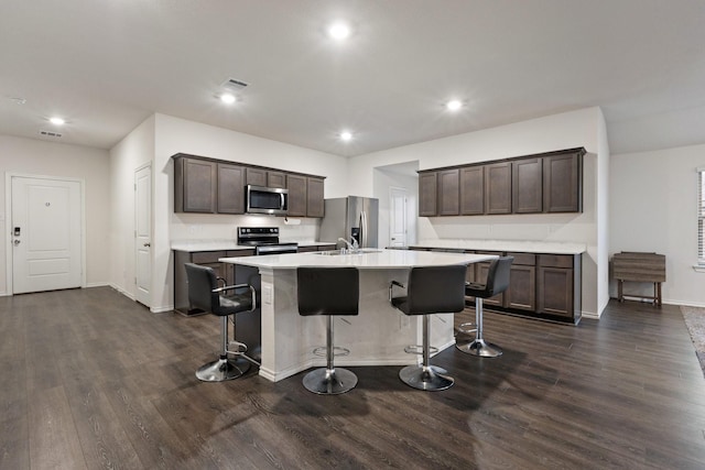 kitchen featuring dark brown cabinets, dark wood-style flooring, stainless steel appliances, and a breakfast bar