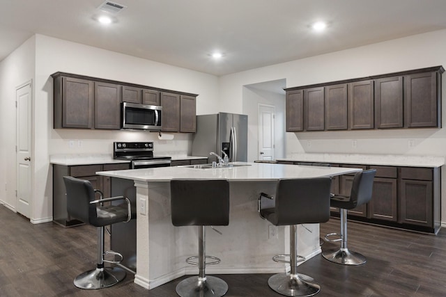 kitchen featuring an island with sink, a sink, dark brown cabinetry, visible vents, and appliances with stainless steel finishes