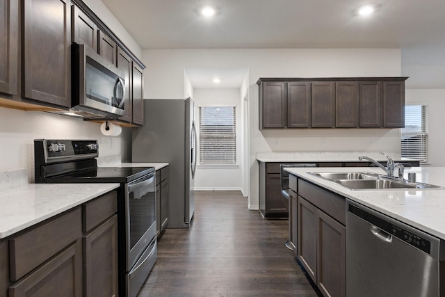 kitchen with a sink, dark wood finished floors, dark brown cabinetry, light stone countertops, and appliances with stainless steel finishes