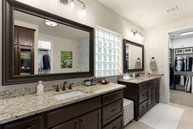 bathroom with a spacious closet, visible vents, two vanities, and a sink