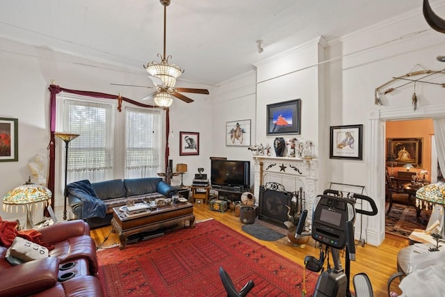 living area featuring a fireplace with flush hearth, ornamental molding, ceiling fan, and wood finished floors