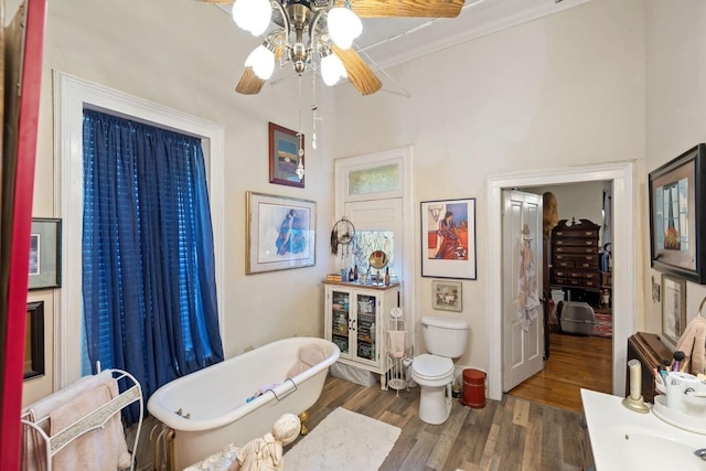 bathroom featuring toilet, wood finished floors, a freestanding bath, crown molding, and ceiling fan