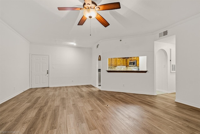 unfurnished living room featuring light wood-style flooring, ornamental molding, ceiling fan, visible vents, and arched walkways
