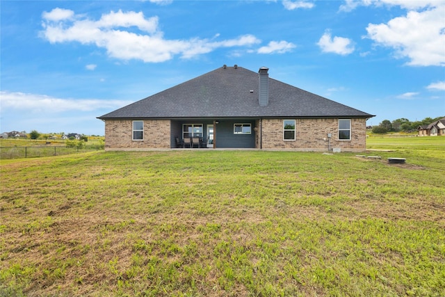 rear view of house with a patio, fence, a lawn, a shingled roof, and brick siding