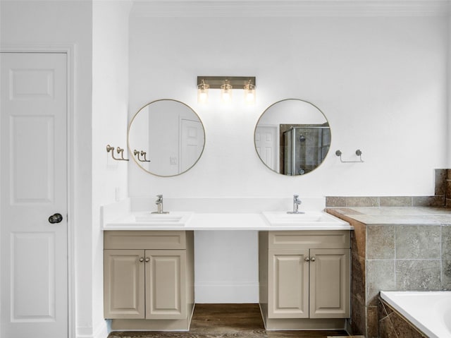bathroom with double vanity, tiled bath, ornamental molding, and a sink