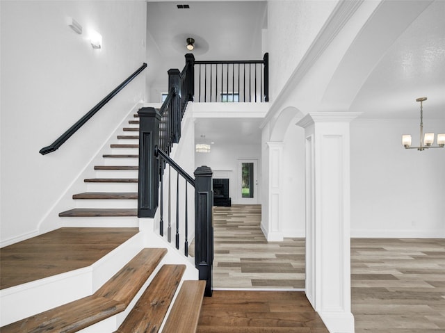 stairs with wood finished floors, decorative columns, a notable chandelier, a towering ceiling, and arched walkways