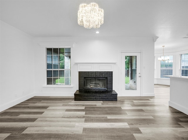 unfurnished living room with a fireplace, an inviting chandelier, baseboards, and wood finished floors