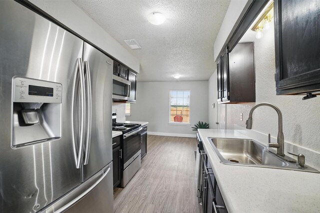 704 Loganwood Dr, Royse City, TX 75189 - kitchen with appliances with stainless steel finishes, a sink, light wood-style floors, a textured ceiling, and light countertops