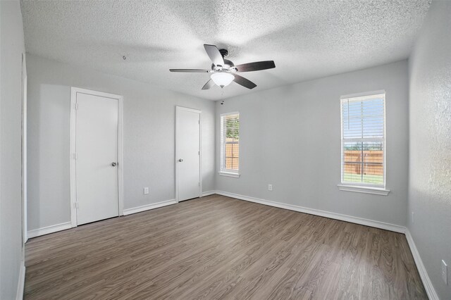 704 Loganwood Dr, Royse City, TX 75189 - unfurnished bedroom featuring wood finished floors, a textured ceiling, baseboards, a ceiling fan, and multiple closets