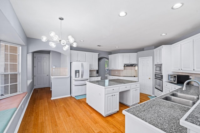 kitchen with white refrigerator with ice dispenser, a sink, oven, arched walkways, and recessed lighting