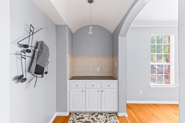 kitchen with white cabinetry, arched walkways, light wood-style flooring, dark countertops, and baseboards