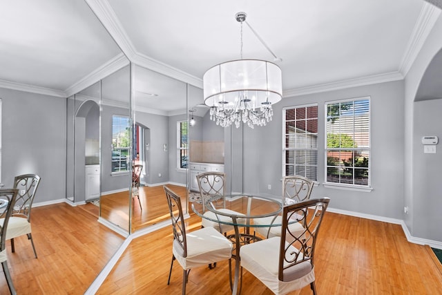dining room featuring arched walkways, plenty of natural light, light wood-style flooring, and crown molding