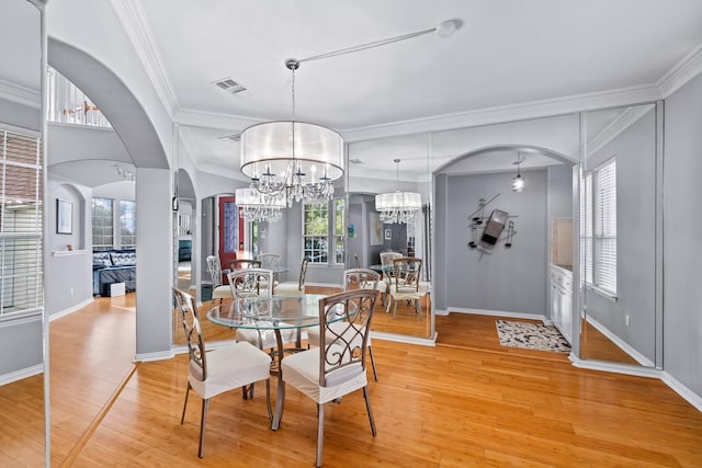 dining room featuring a chandelier, arched walkways, light wood finished floors, ornamental molding, and baseboards