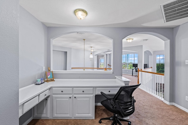 unfurnished office featuring carpet flooring, arched walkways, and baseboards