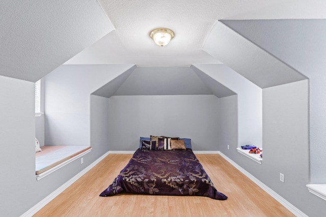 bedroom featuring wood finished floors, lofted ceiling, a textured ceiling, and baseboards