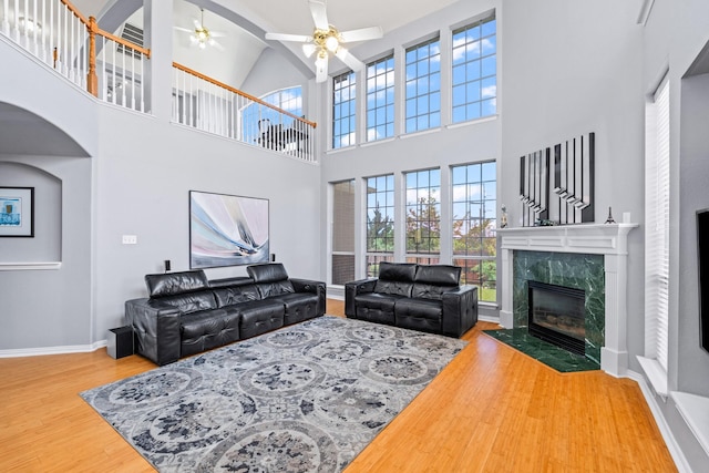 living area featuring wood finished floors, a high ceiling, a ceiling fan, a premium fireplace, and baseboards