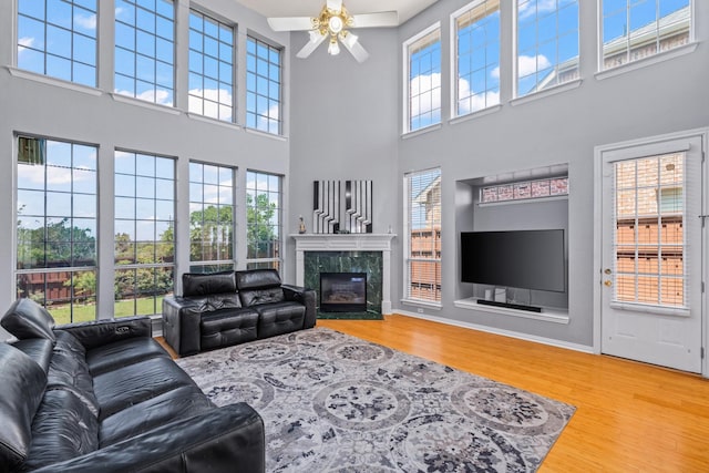living room featuring a ceiling fan, wood finished floors, a high ceiling, and a premium fireplace