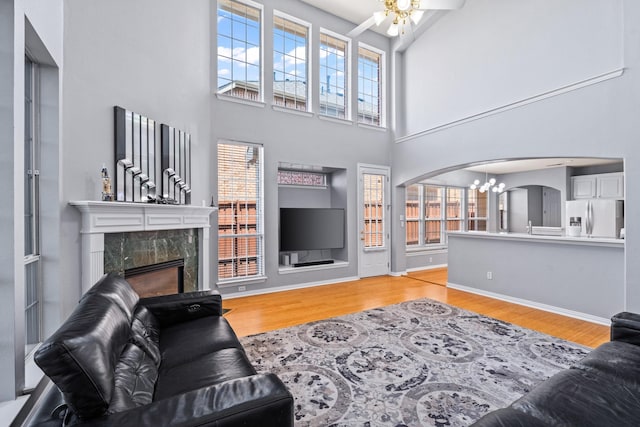 living area featuring a chandelier, a premium fireplace, arched walkways, a towering ceiling, and light wood-type flooring