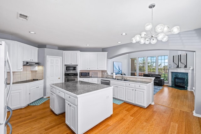 kitchen with stainless steel appliances, a peninsula, a center island, arched walkways, and a sink