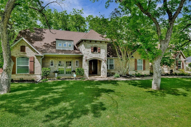 view of front of property featuring stone siding, a shingled roof, french doors, and a front lawn