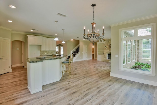 kitchen featuring ornamental molding, visible vents, light wood-style flooring, arched walkways, and baseboards