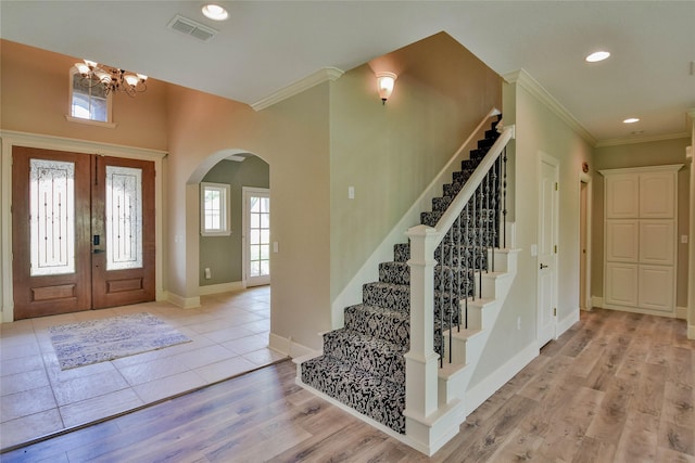 foyer entrance featuring a notable chandelier, visible vents, arched walkways, ornamental molding, and stairs
