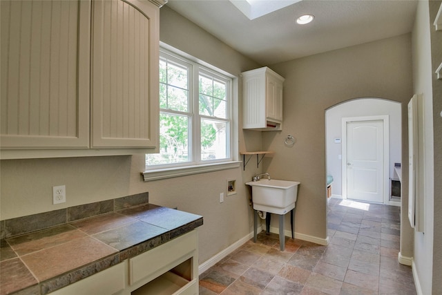 laundry area featuring stone tile floors, washer hookup, arched walkways, and plenty of natural light