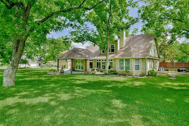 rear view of house featuring a chimney, a yard, brick siding, fence, and a patio