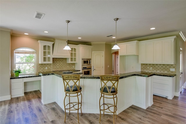 kitchen with light wood finished floors, backsplash, glass insert cabinets, custom range hood, and appliances with stainless steel finishes