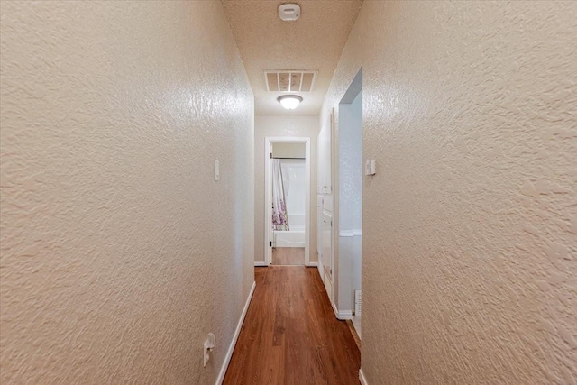 hall with a textured wall, baseboards, visible vents, and wood finished floors