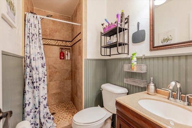 full bath featuring vanity, toilet, wainscoting, and tiled shower