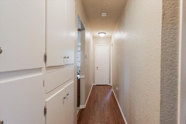hall featuring baseboards, dark wood-type flooring, a textured ceiling, and a textured wall