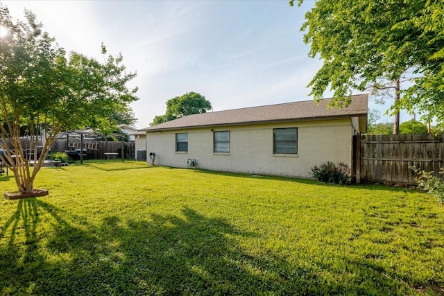 back of house featuring a fenced backyard, brick siding, and a lawn