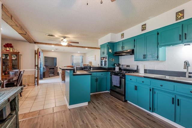 kitchen with under cabinet range hood, ceiling fan, a sink, a peninsula, and stainless steel range with gas stovetop