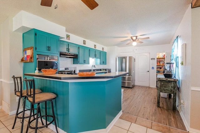 kitchen with under cabinet range hood, freestanding refrigerator, a peninsula, and a ceiling fan