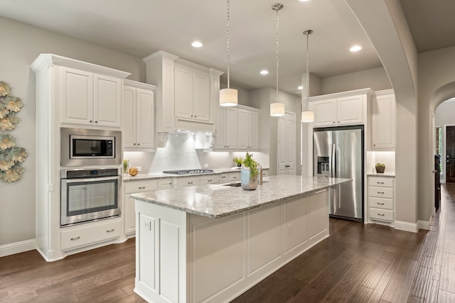 kitchen with a kitchen island with sink, dark wood-type flooring, arched walkways, white cabinets, and appliances with stainless steel finishes