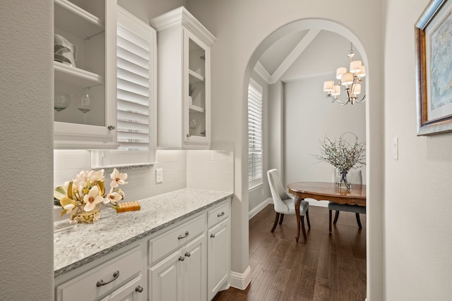 bar with a notable chandelier, dark wood-type flooring, baseboards, arched walkways, and tasteful backsplash