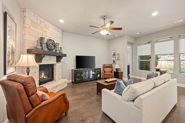 living room with a ceiling fan, a stone fireplace, visible vents, and dark wood-type flooring