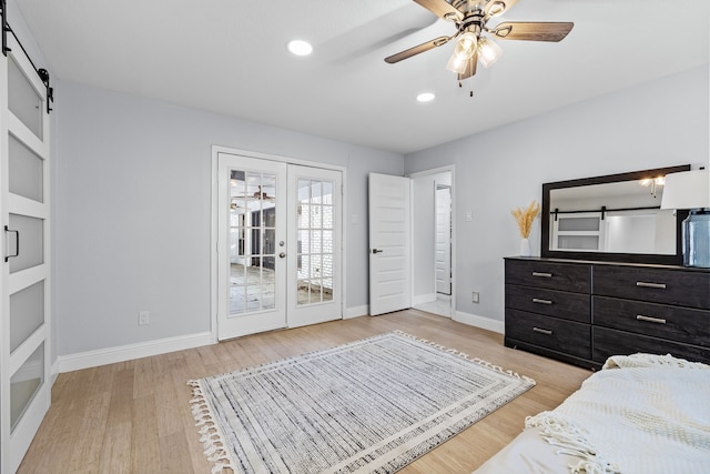 bedroom with baseboards, french doors, a barn door, and light wood-style flooring