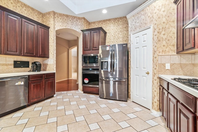 kitchen featuring wall chimney range hood, stainless steel appliances, arched walkways, light countertops, and decorative backsplash