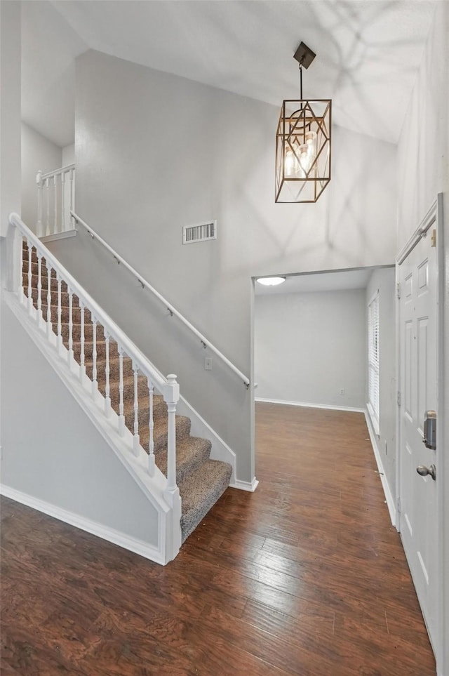 foyer entrance featuring a notable chandelier, baseboards, visible vents, stairs, and wood finished floors
