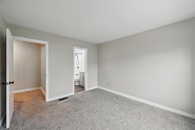 unfurnished bedroom featuring baseboards, ensuite bathroom, visible vents, and carpet