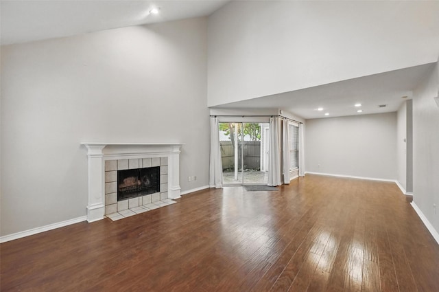 unfurnished living room with wood finished floors, a tiled fireplace, baseboards, a towering ceiling, and recessed lighting