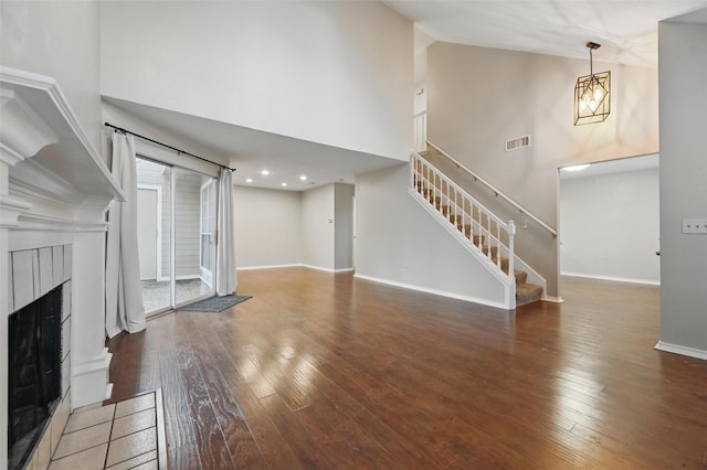 unfurnished living room with wood-type flooring, high vaulted ceiling, a fireplace, visible vents, and stairs